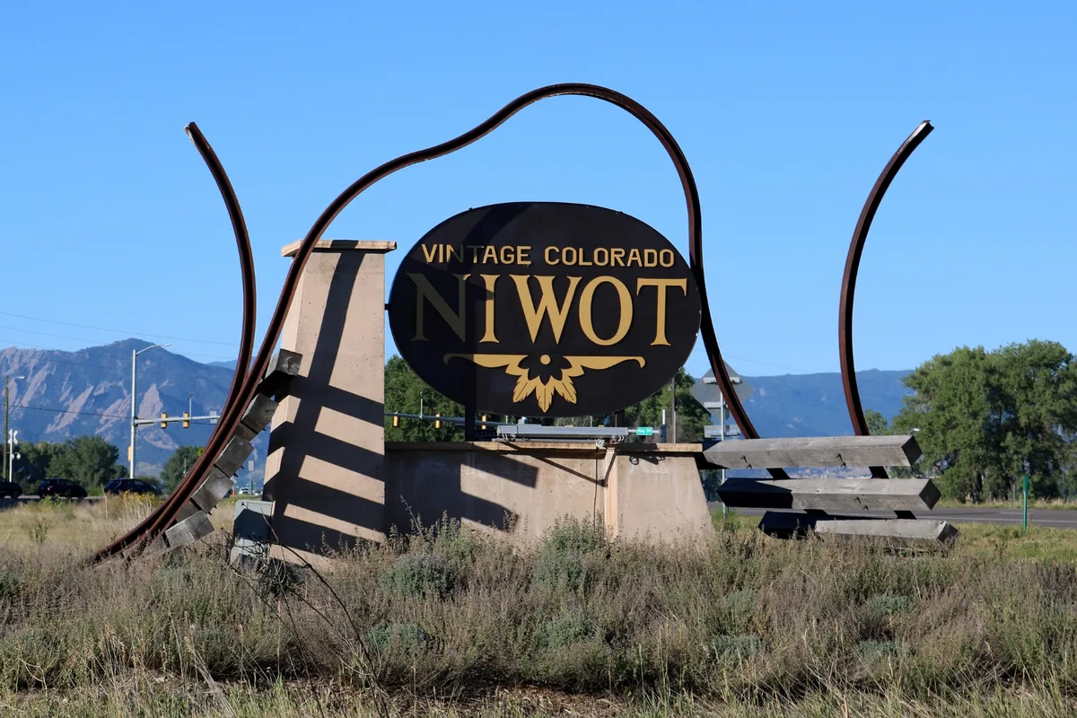 The steel gateway sculpture at the highway edge of Niwot: an oval sign held inside two curving rails