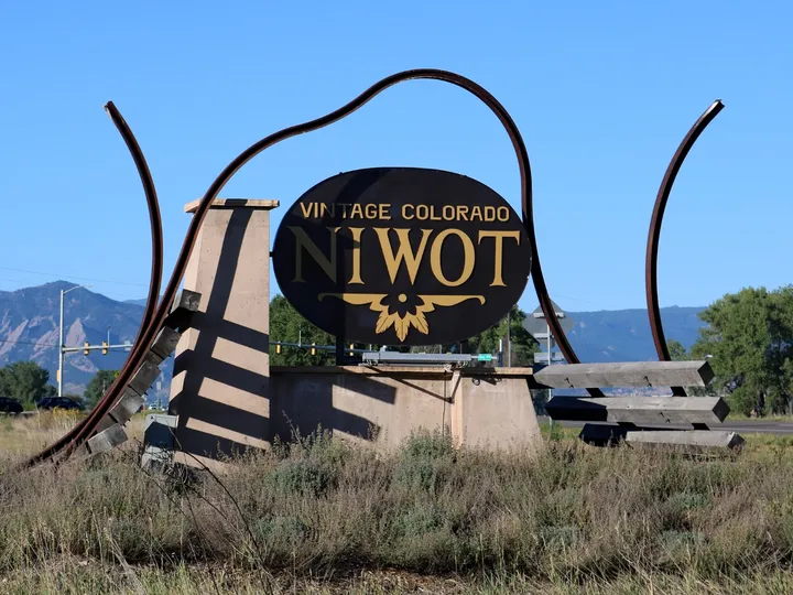 The steel gateway sculpture at the highway edge of Niwot: an oval sign held inside two curving rails